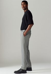 T-shirt noir à manches courtes associé à un pantalon gris clair et des chaussures à lacets noires. La tenue présente une coupe décontractée et des textures lisses.