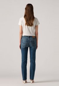 Lichtgrijze, korte mouwen t-shirt in combinatie met blauwe, strakke denim jeans. De jeans hebben achterzakken met stiksel details en een bruine leren label.
