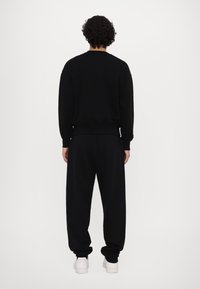 Sudadera negra y joggers a juego hechos de una tela suave, con puños y cintura acanalados. Diseño simple sin patrones visibles ni acentos.