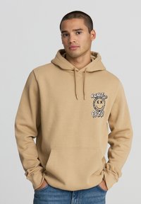 Felpa beige in cotone misto. Presenta una tasca frontale e un design grafico con testo e faccina sorridente nella zona sinistra del petto. Vestibilità regolare.