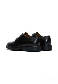 Zwarte leren dresschoenen met een gladde structuur, ronde neuzen en lage hakken; voorzien van veters en subtiele stikseldetails.