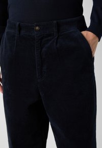 Navy kendernadrág, amely texturált bordázott mintázattal, elülső zsebekkel és egy gombos záródással rendelkezik a derékon.