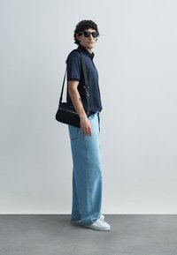 Ναυτικό πόλο πουκάμισο, ανοιχτό μπλε τζιν με φαρδιά φέτα, μαύρη τσάντα χιαστί, λευκά αθλητικά παπούτσια και σκούρα γυαλιά ηλίου. Ομαλά υφάσματα και απλός σχεδιασμός.