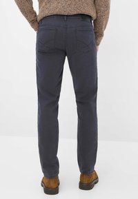 Jeans dritti blu scuro con tasche posteriori che mostrano accenti di cucitura. Tessuto in cotone misto morbido, design informale e finitura pulita.