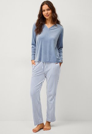 Top lungo a maniche con scollo a V in velluto blu, abbinato a pantaloni a righe bianchi e azzurri con tasche laterali. Tessuto morbido, vestibilità casual.