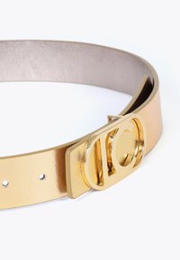 Guld läderbälte med en glansig yta, utrustad med en framträdande guldlogo-spänne. Slät textur och klassisk spänndesign.