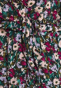 Blommönstrad tyg i mörkgrön med rosa, vita och lavendelfärgade blommor; har en knytmidja och lager av volangdetaljer i nederkant.