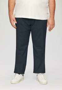 Pantalon en denim bleu foncé à coupe droite, associé à des baskets blanches décontractées. Le tissu a une texture lisse et montre peu de coutures visibles.