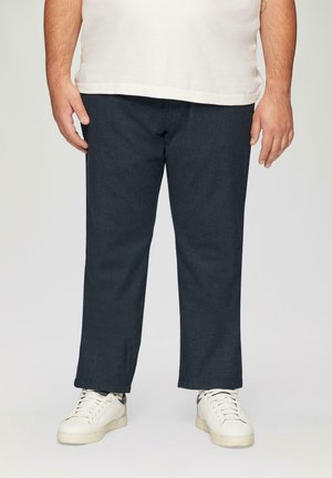 Donkerblauwe denim broek met een rechte snit, gecombineerd met witte casual sneakers. De stof heeft een gladde textuur en minimale zichtbare naden.