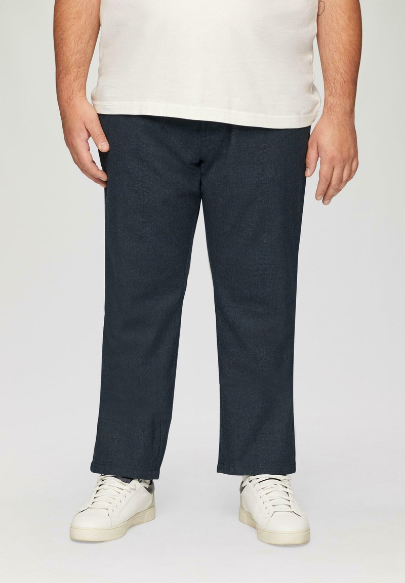 Pantalon en denim bleu foncé à coupe droite, associé à des baskets blanches décontractées. Le tissu a une texture lisse et montre peu de coutures visibles.