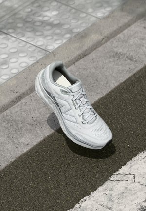 White athletic shoe with a mesh upper, rubber sole, and textured design. Features grey accents and laces with breathable elements.