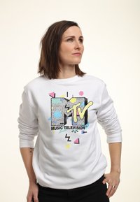 Bílá mikina s barevným logem MTV, které obsahuje geometrické vzory v růžových, žlutých a modrých odstínech. Měkká, texturovaná tkanina.