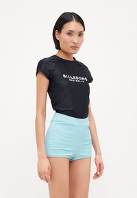 Schwarz kurzärmliges Shirt mit dem Text "BILLABONG AUSTRALIA", kombiniert mit hellblauen, gerippten hochgeschnittenen Shorts. Glattes Material, figurnaher Schnitt.