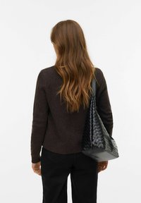 Melnā austā ādas soma ar vaļīgu dizainu, nēsāta pāri tumši brūnam džemperim. Somai ir teksturēta virsma un plakans pamatne.