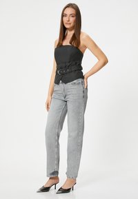 Top negro sin tirantes con cintura ceñida, combinado con jeans rectos de color gris claro y tacones negros de punta en un fondo liso.