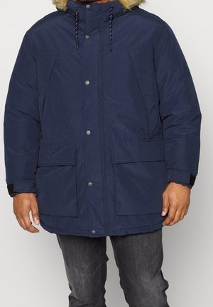 Abrigo acolchado de color azul marino con capucha forrada de piel, botones de presión en la parte frontal, dos grandes bolsillos frontales y cordones ajustables en el cuello.