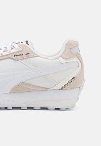 Sneaker con una parte superiore in pelle bianca e dettagli in suede beige, suola in gomma testurizzata e cuciture a contrasto.