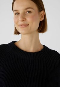 Dunkelblauer Strickpullover mit gerippter Textur, weitem Rundhalsausschnitt und sichtbarem Zopfmuster. Nahaufnahme des Oberteils.