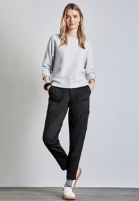 Ljusgrå stickad tröja med rullade ärmar, tillsammans med svarta tapered joggare med två framfickor. Bärs med vita skor.