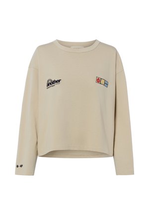 Beige long-sleeve cropped sweatshirt with black "another" text on left chest and three small colorful patch designs on right chest and small flower prints on left sleeve cuff.