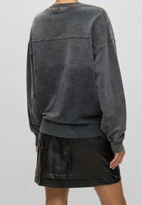 Př oversized šedou mikinu s vybledlou texturou a žebrovanými manžetami, kombinovanou s černou lesklou koženou mini sukňou s viditelným švem.