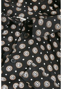 Chemise noire avec des pois blancs et des motifs circulaires en orange et blanc. Dotée d'un col pointu et de deux boutons noirs.