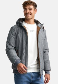 Gray puffer jacket with a hood, featuring brown accents, a front zipper, elastic cuffs, and a casual fit, layered over a white shirt.