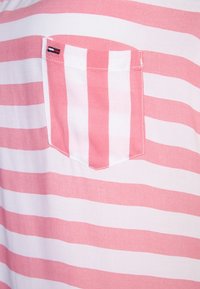 Rosa och vit randig tyg med en fickdetalj. Ränderna är jämnt fördelade, och fickan har en liten märkesetikett.