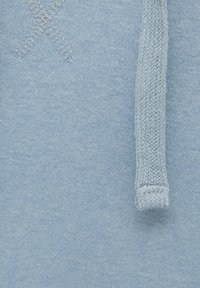 Tissu tricoté bleu clair avec une texture douce. Comprend un cordon tissé et un motif "X" cousu pour le détail.