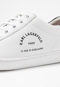 Bílé kožené tenisky s kulatou špičkou, šněrovacím designem a potištěnými detaily značky, včetně „Karl Lagerfeld“, „Paříž“ a adresy.