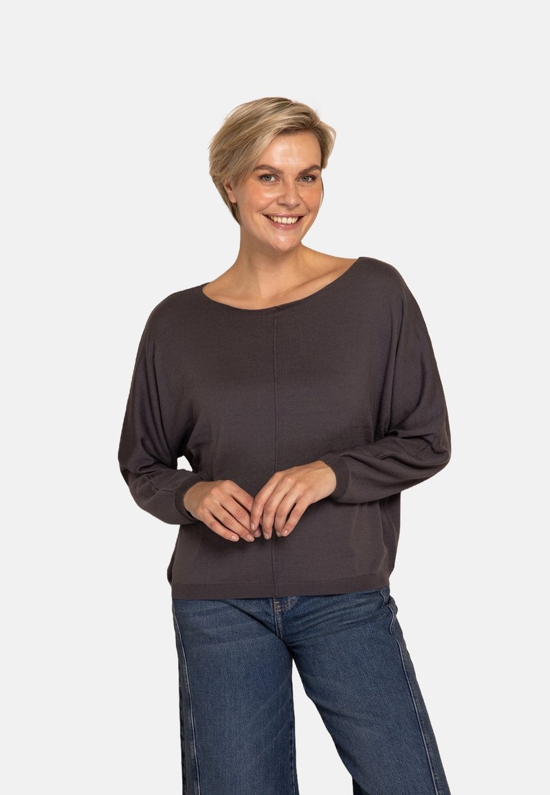 Dunkelgrauer Pullover mit weitem Ausschnitt, langen Ärmeln und gerippter Struktur, kombiniert mit blauen Jeans mit weitem Bein. Einfaches, entspanntes Design.