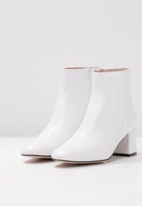 Bottines blanches en cuir avec un bout pointu et un talon carré. Elles sont dotées d'une fermeture éclair latérale et d'une texture lisse avec des détails de couture minimalistes.