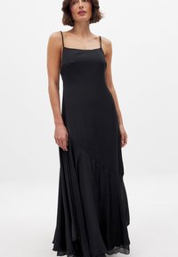 Musta, hihaton maksimekko, joka on valmistettu sileästä kankaasta. Mekossa on istuva yläosa ja leveä helma kerroksellisella muotoilulla, joka lisää liikettä.