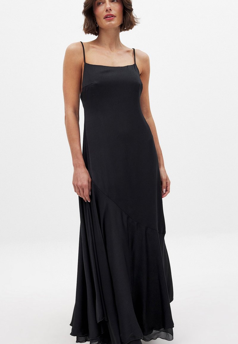 Musta, hihaton maksimekko, joka on valmistettu sileästä kankaasta. Mekossa on istuva yläosa ja leveä helma kerroksellisella muotoilulla, joka lisää liikettä.