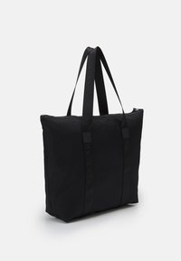 Borsa tote nera in nylon con doppi manici, apertura con zip, forma piatta e dettagli del logo del brand impresso sui manici. Texture liscia.