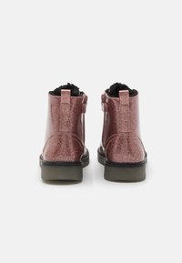 Glitrende rosa ankelstøvler med en glatt tekstur, svart faux pelsforing, og gummisåle. Har en trekkflik og justerbar stroppdetalj.