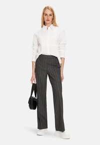 White button-up shirt with rolled sleeves, paired with dark gray pinstriped trousers. Shoes are white platform sneakers; carrying a black handbag.