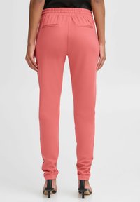 Růžové jogger kalhoty s elastickým pasem a slim fit, mají dvě zadní kapsy a hladkou texturu látky. Stylizované s černými lodičkami.