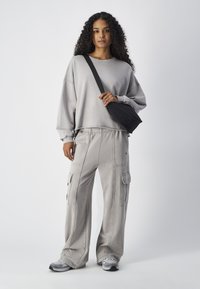 Lichtgrijze oversized sweatshirt met drop shoulders, gecombineerd met lichtgrijze cargobroek met zijzakken en een zwarte crossbody tas.