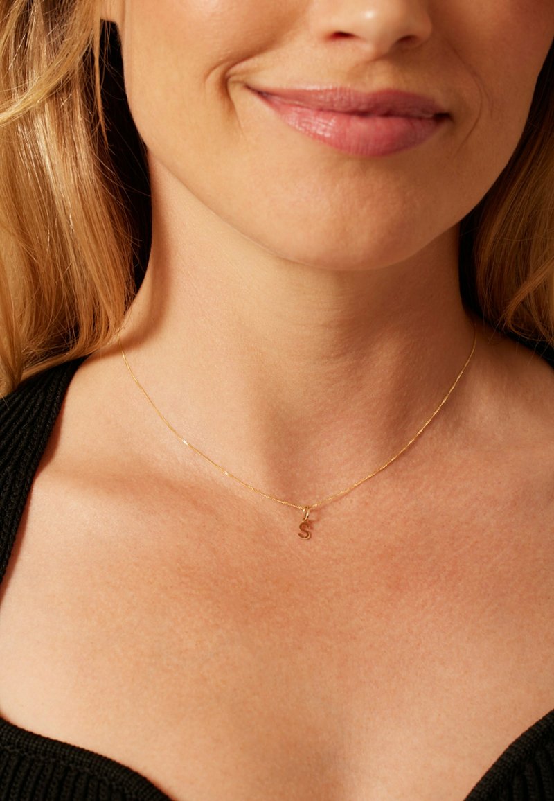 Goldkette mit einer filigranen Kette und einem kleinen „S“-Anhänger. Die Kette ist fein und glatt, ergänzt durch ein minimalistisches Design.