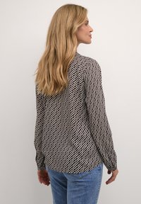 Camicia a maniche lunghe con un motivo geometrico in bianco e nero, realizzata in tessuto leggero, con un fit rilassato e polsini bottonati.