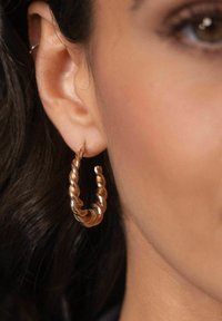 Kupferne, gedrehte Creole, die am Ohr getragen wird, mit einem spiralförmigen Design und glatter Textur, die ihren metallischen Glanz und ihre Form betont.