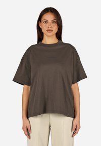 Czarna szara, oversize koszulka z okrągłym dekoltem i krótkimi rękawami, wykonana z miękkiej bawełnianej tkaniny, z subtelnym logo na wysokości klatki piersiowej.