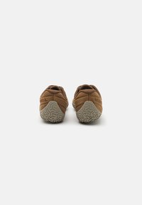 Brown suede shoes with a textured grey rubber sole. Features a rounded back with embossed brand name. Dual-tone design and minimalistic shape.