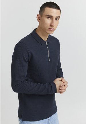 Navy long-sleeve polo shirt with a textured pattern, half-zip closure, and a contrasting collar. Side slits at the hem for comfort.