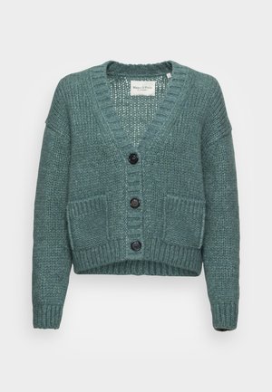 Cardigan tricoté épais couleur sarcelle avec trois boutons noirs, manches longues, col en V, deux poches avant et poignets et ourlet côtelés.