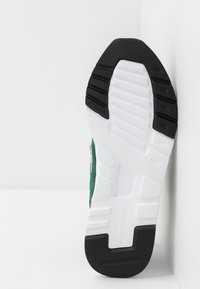 Zelené tenisky s texturovaným nubukovým svrškem, bílou mezipodešví a černou gumovou podešví s dezénem pro lepší přilnavost.