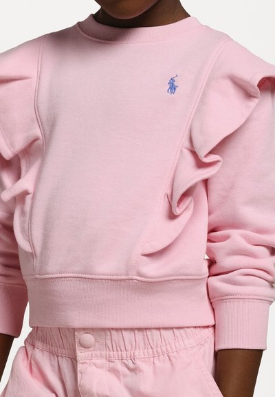 Rosa sweatshirt med volangdetaljer på ärmarna, stickad textur och rundad krage. Har en liten blå broderad logotyp på bröstet.
