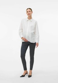 Chemise blanche à manches longues, associée à un pantalon slim-fit gris à carreaux et des chaussures à talons noires. Design simple et classique.
