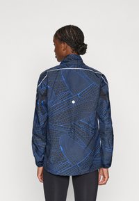 Lichte zwarte jack met een blauw geometrisch patroon, hoge kraag en elastische manchet, met reflecterende accenten voor zichtbaarheid.